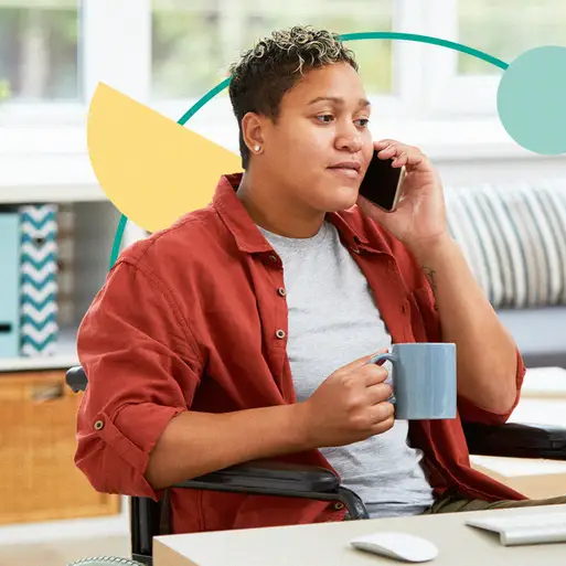 Person sitting at a desk, holding a mug in their right hand, and talking on their mobile phone.